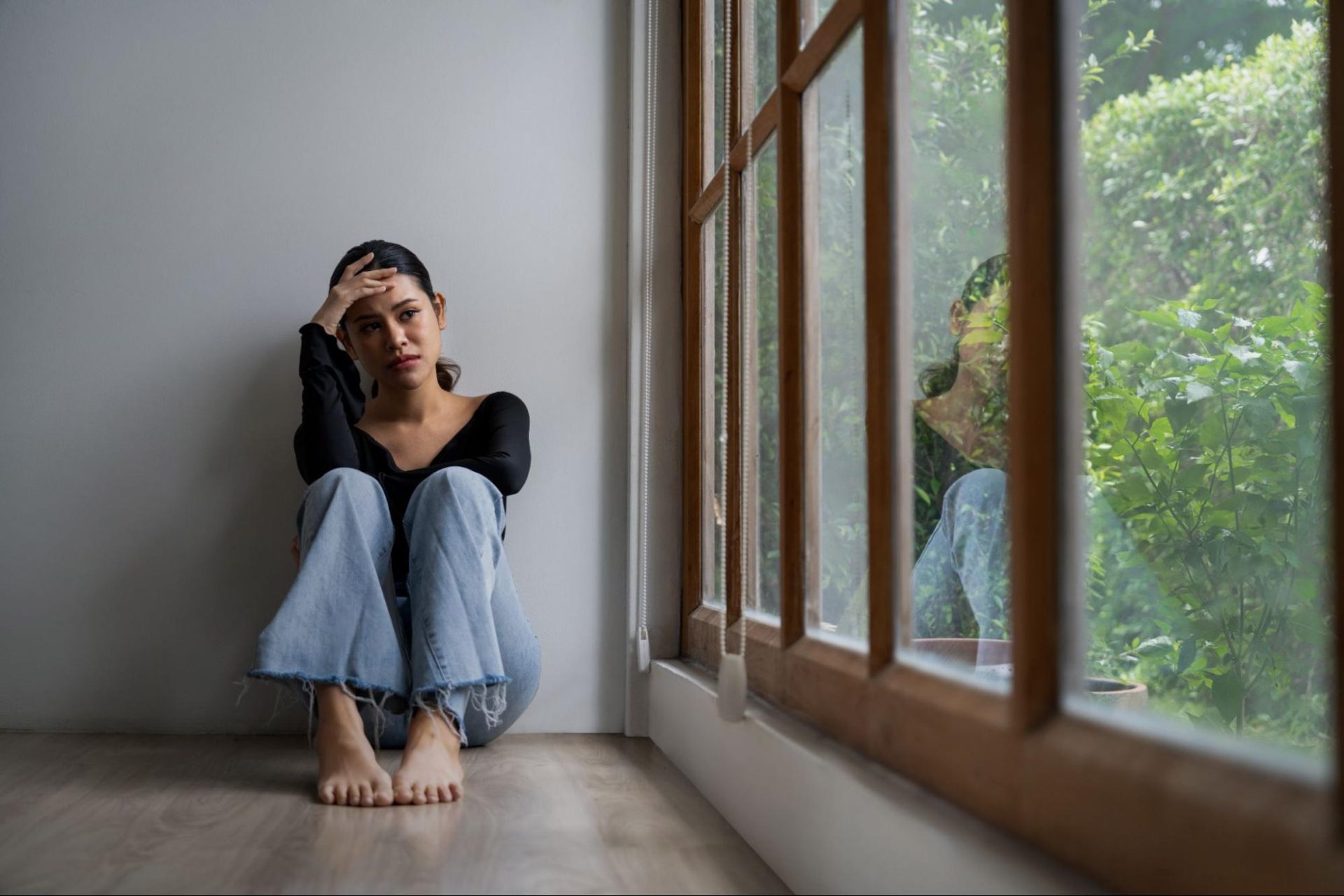 Sad young woman sitting on floor looking out a window.