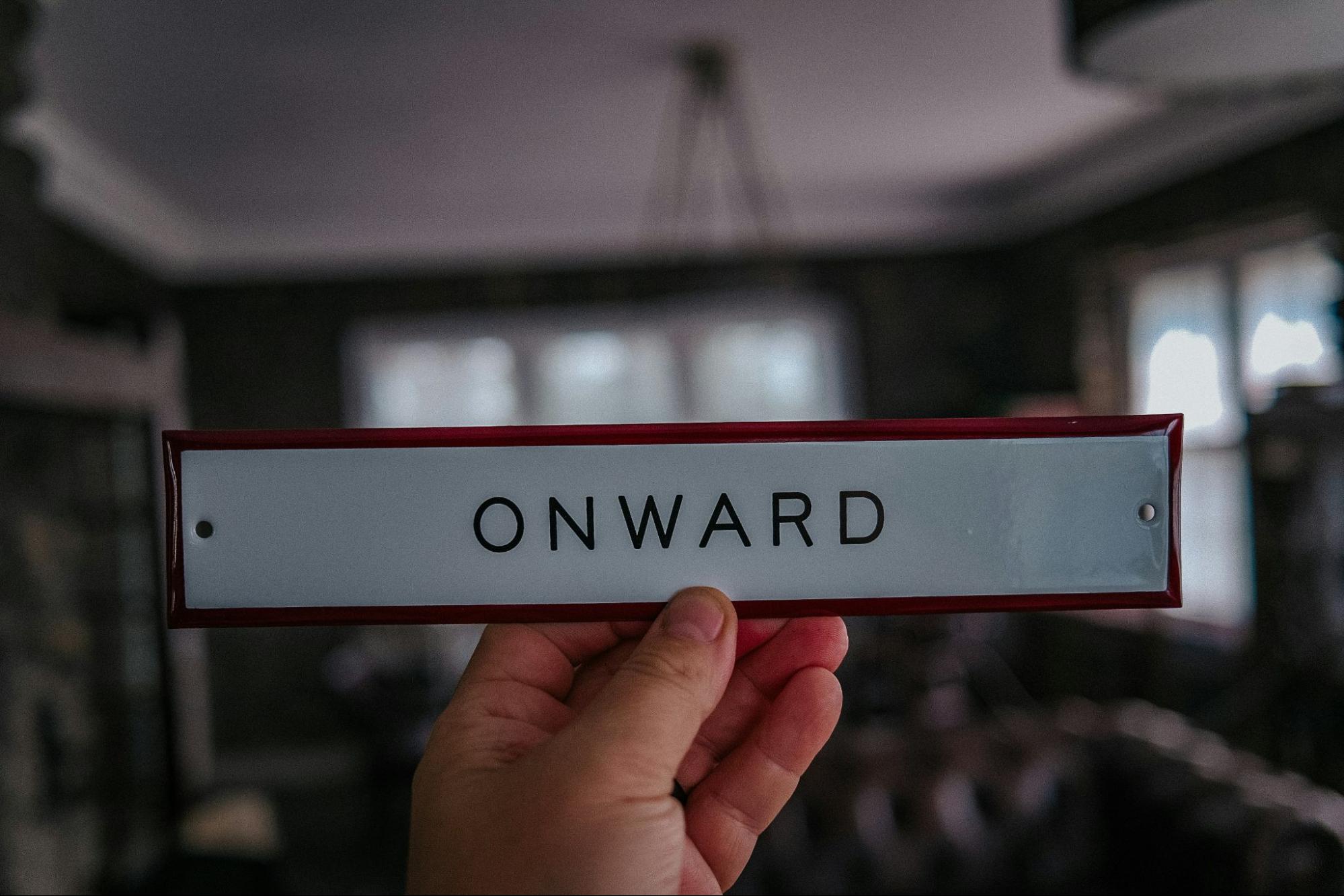 Hand holding what looks like a door name plate that says ONWARD.