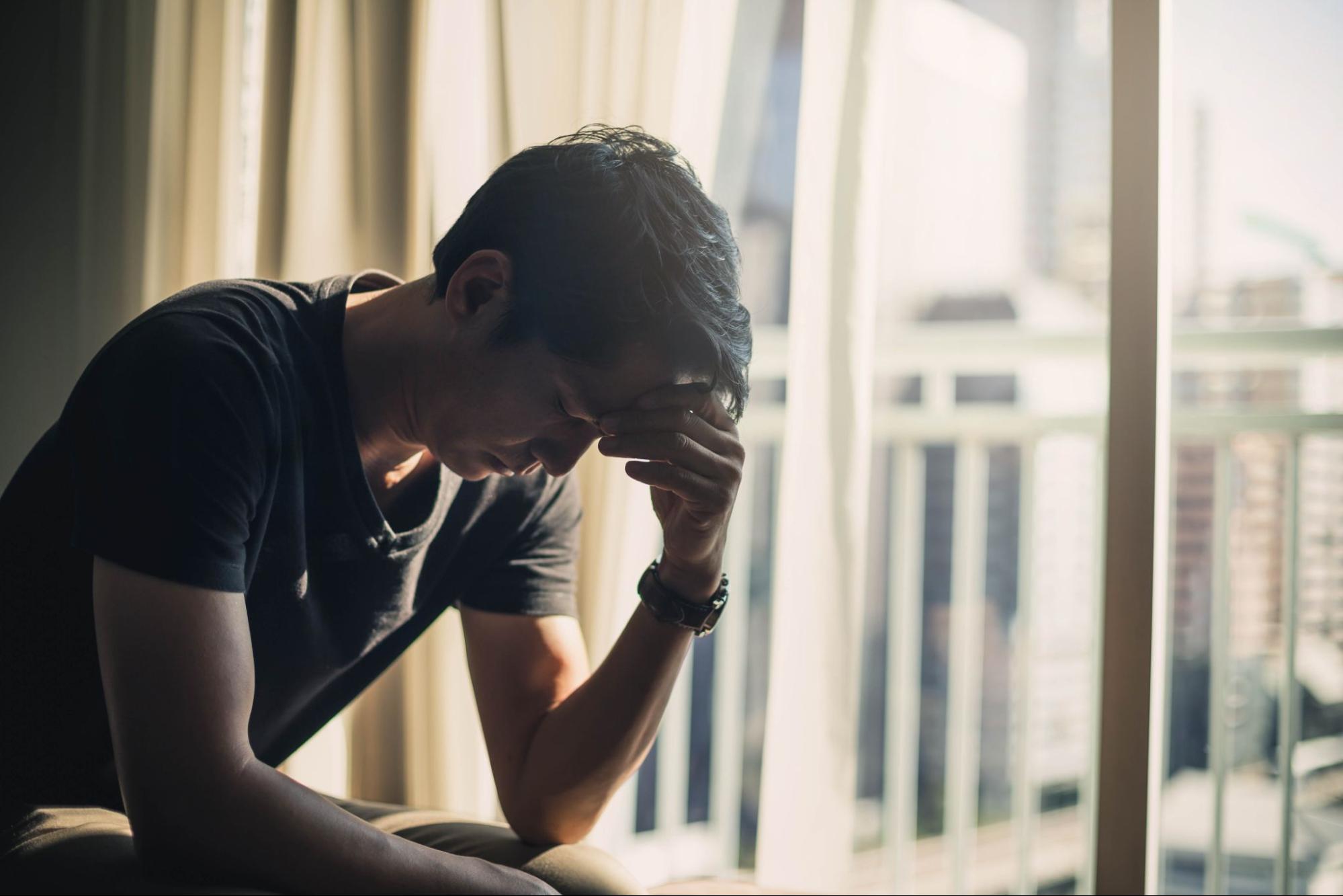 Man sitting alone sad on his bed with his hand to forehead. 