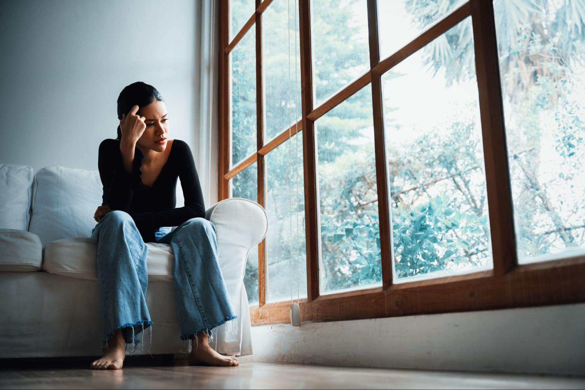 Young woman sitting and looking outside of window pondering a difficult decision. 