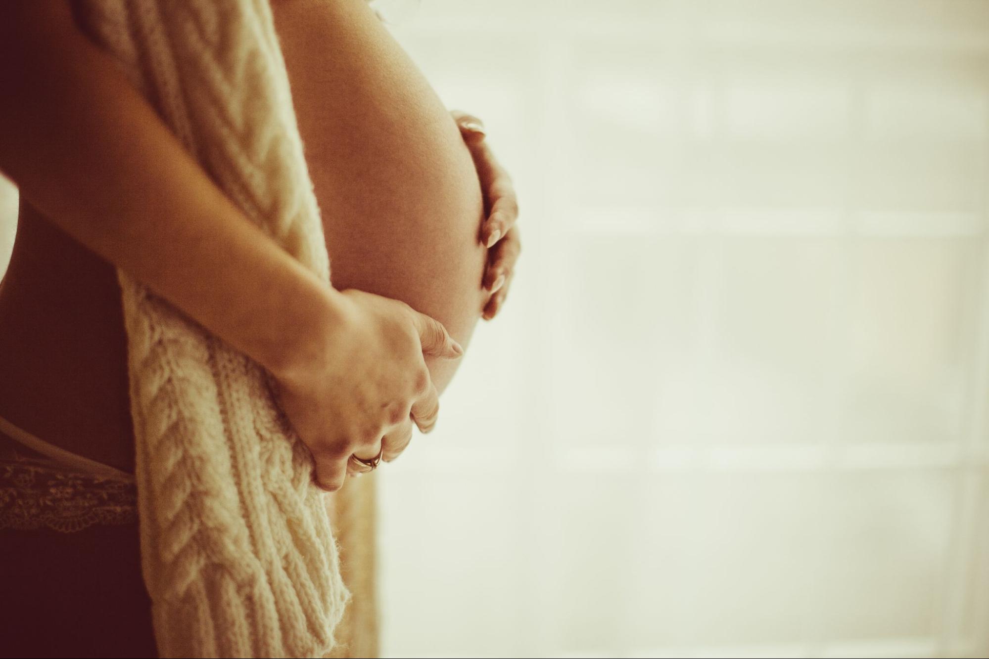 Pregnant woman cradling her bare belly. 