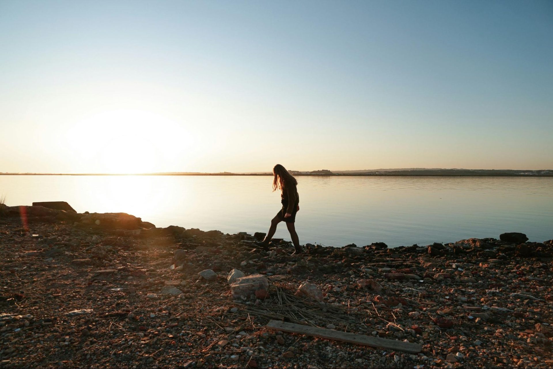 Woman walking along the rocks on the shore of the ocean at sunrise.