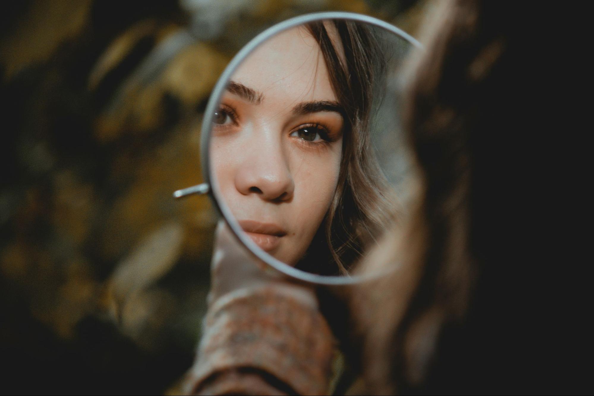 Young brunette woman looking into mirror and smiling. 