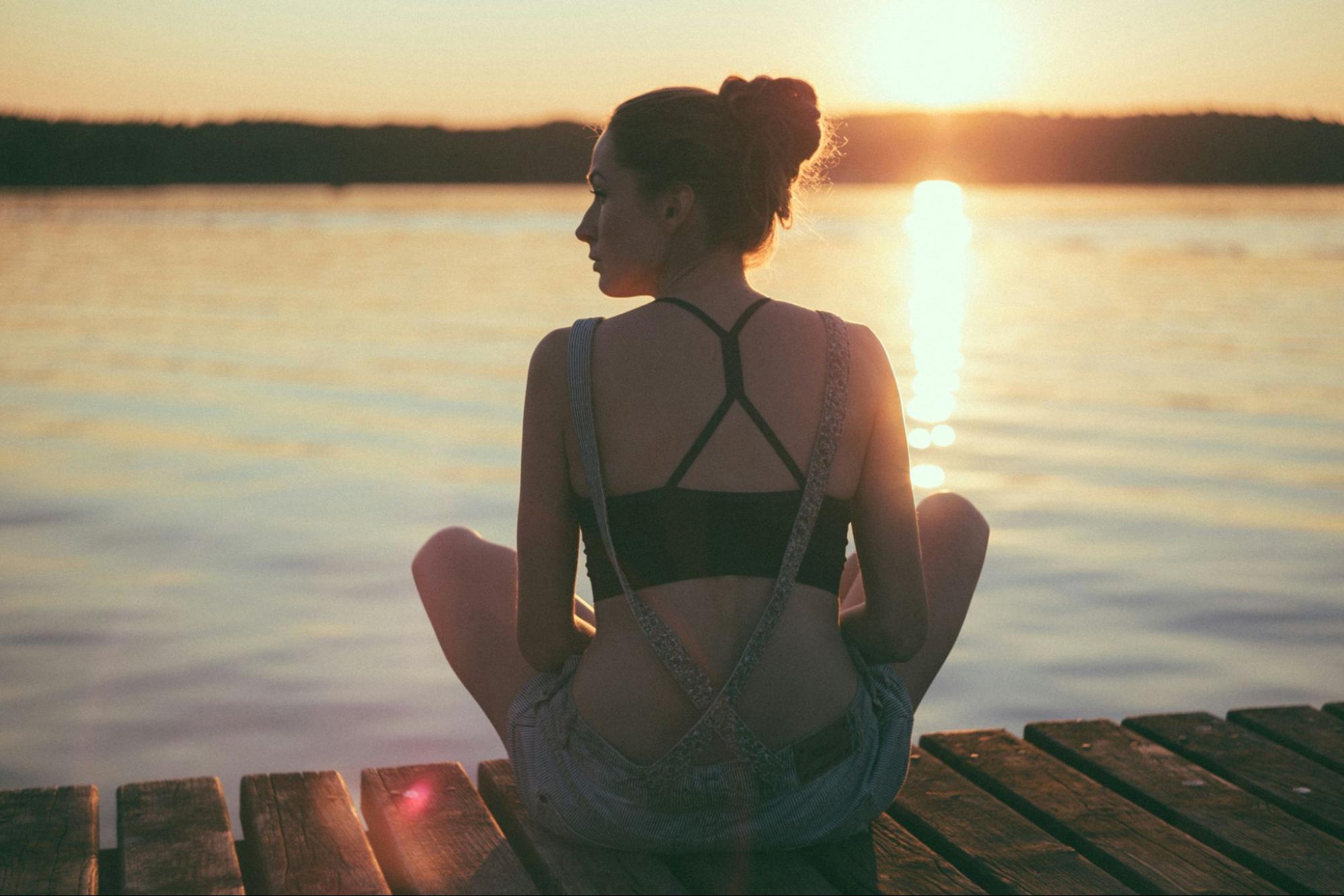 Woman sitting crosslegged on pier in front of the the sun rising over the water.