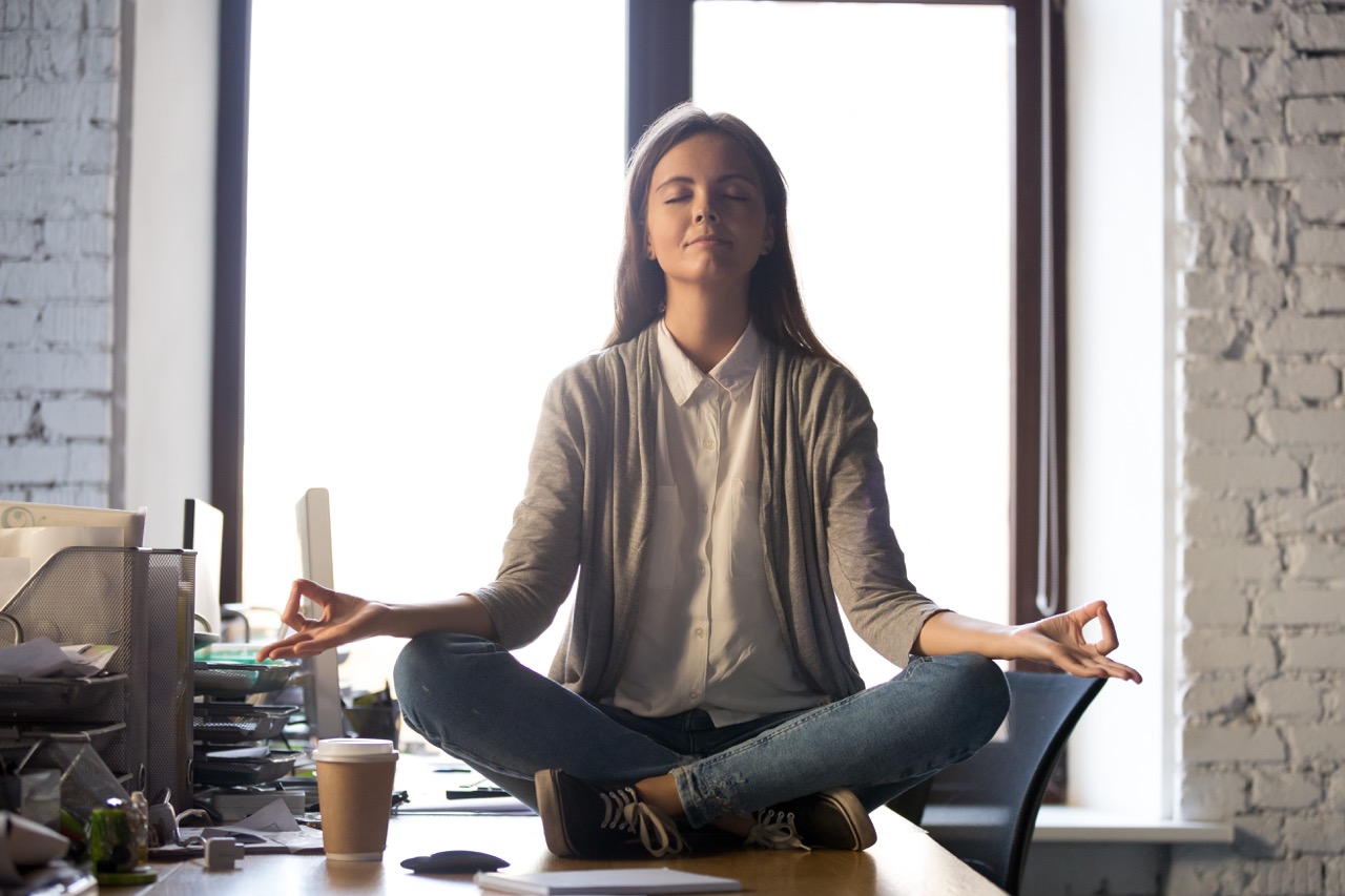 Woman sitting on top of desk with legs crossed, meditating.